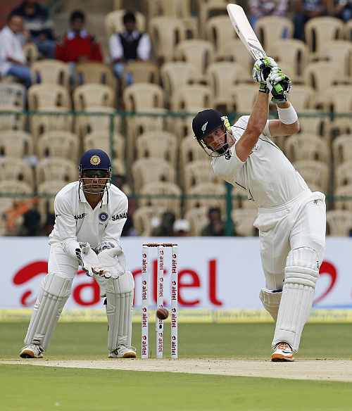 New Zealand's Martin Guptill hits a shot as MS Dhoni watches on during the first day of their second Test match in Bangalore