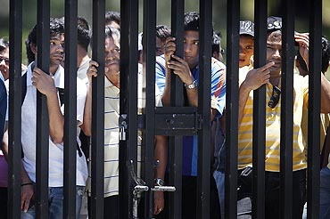 Indian cricket fans peer through the bars of a fence next to the nets area to try and catch a glimpse of the Indian cricket team members during a practice session on Monday
