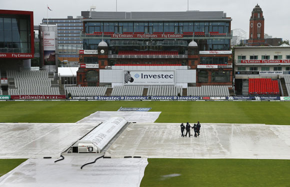 Ground staff brush water off the covers as rain falls on the pitch