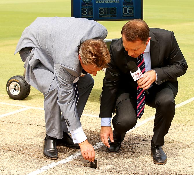 Television commentators Ian Healy (left) and Michael Slater place a mobile phone into a crack on the pitch before start of play on day four