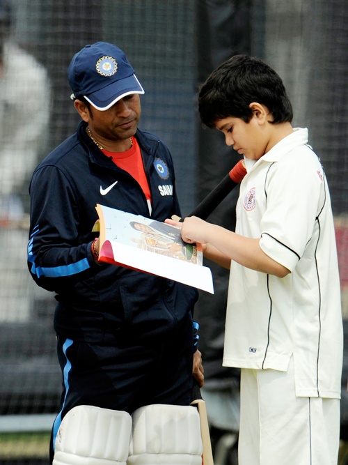 India's Sachin Tendulkar looks at a book with his son Arjun