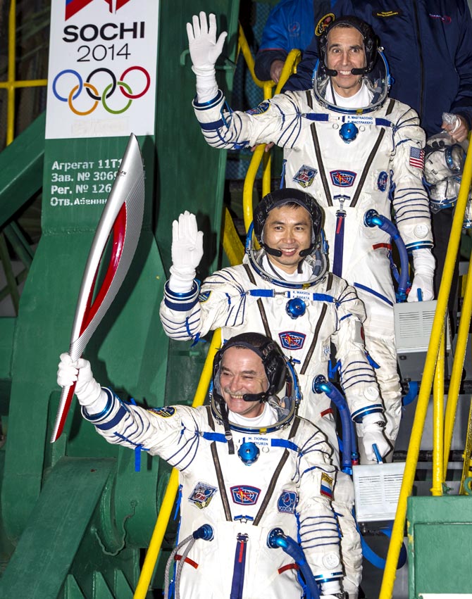 Expedition 38 Soyuz Commander Mikhail Tyurin of Roscosmos, holding the Olympic torch, Flight Engineer Koichi Wakata of the Japan Aerospace Exploration Agency, and, Flight Engineer Rick Mastracchio of NASA (top), wave farewell prior to boarding the Soyuz TMA-11M rocket for launch