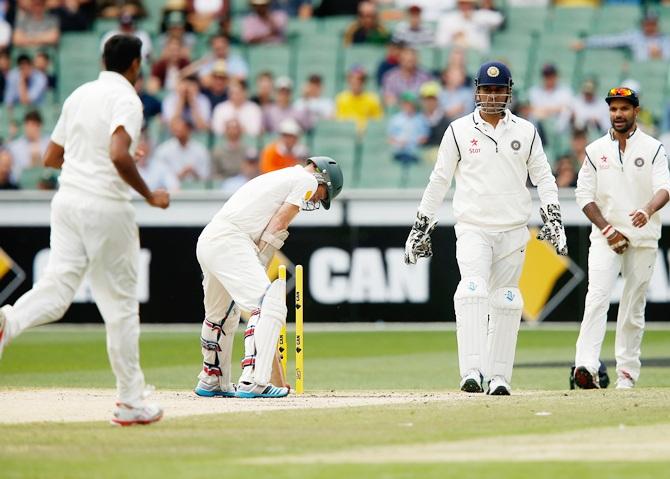 Chris Rogers of Australia hunches over his bat as Indian players celebrate his dismissal