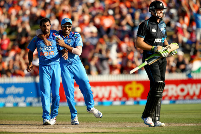 Martin Guptill of New Zealand walks off as Mohammed Shami (left) and Rohit Sharma of India celebrate his dismissal