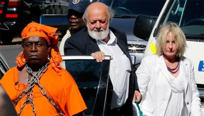 A protester with chains (left) looks on as Barry (centre) and June Steenkamp, the parents of Reeva Steenkamp arrive at the North Gauteng High Court in Pretoria