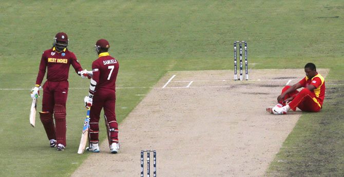 Zimbabwe's bowler Tinashe Panyangara (right) sits on the pitch after being hit for four runs by Marlon Samuels as he fist-bumps with teammate Chris Gayle