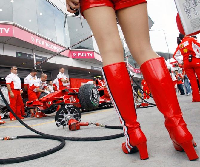 A race queen stands next to a Ferrari Formula One car at the pit