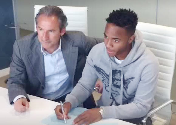 Raheem Sterling sits with a Manchester City official as he signs on the dotted line