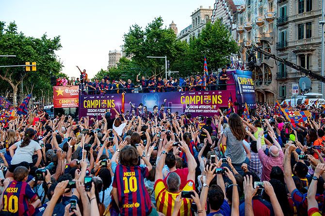 Fans watch as FC Barcelona players celebrate on an open-top bus during their victory parade