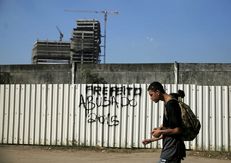 Residents of the Vila Autodromo favela walk in front of the construction work for the Rio 2016 Olympic Park in Rio de Janeiro on Monday