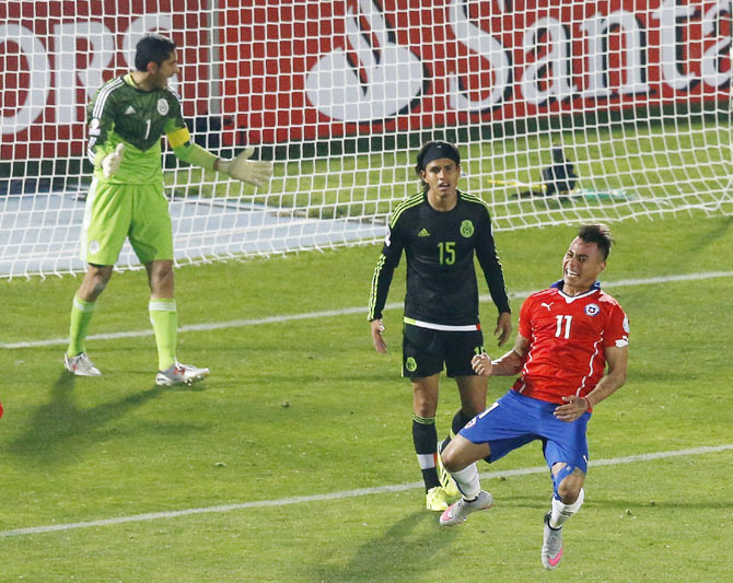 Chile's Eduardo Vargas celebrates after scoring against Mexico's goalie Jose Corona as Mexico's Gerardo Flores looks on during their first round Copa America 2015 match at the National Stadium in Santiago, Chile on Monday