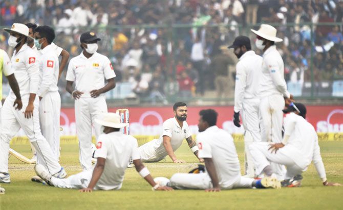 India captain Virat Kohli stretches while play is held up while Sri Lanka players wear anti-pollution masks on Day 2 of the 3rd Test at Feroz Shah Kotla in New Delhi on Sunday
