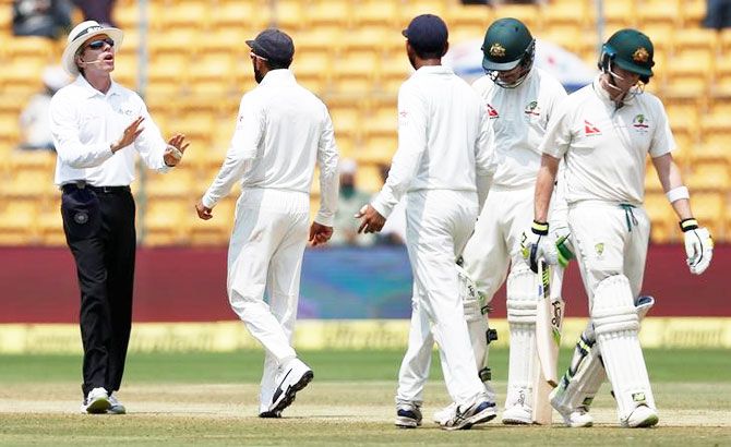 India's captain Virat Kohli (2nd from left) speaks to the umpire as Australia's captain Steven Smith (right) walks off the ground after being dismissed on Day 4 of the 2nd Test in Bengaluru on Tuesday