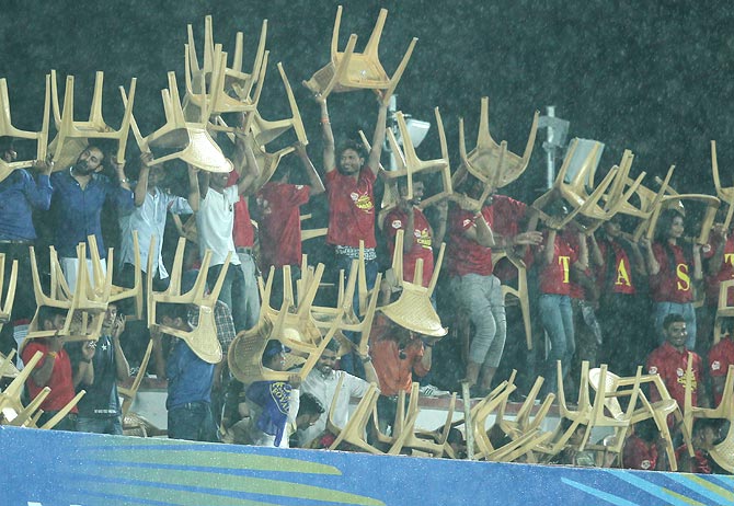 Spectators use plastic chairs in the stands to take shelter from the rain