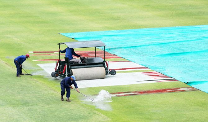 Ground staff workers at Newlands Stadium try to sweep water on the pitch