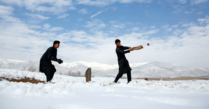 Afghan men play cricket on a field covered in snow on the outskirts of Kabul, Afghanistan