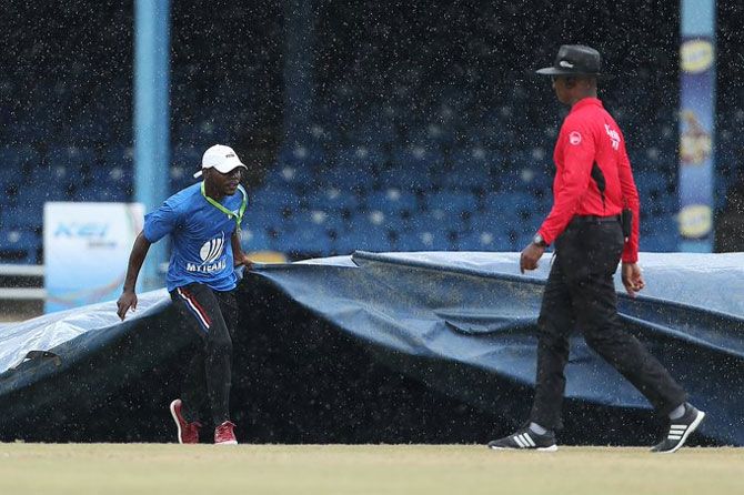 A groundsman runs in with the covers as rain interrupts play during the India innings