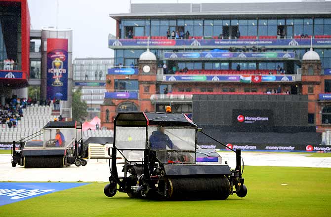 Ground staff work to dry the pitch dry as play is delayed due to rain.