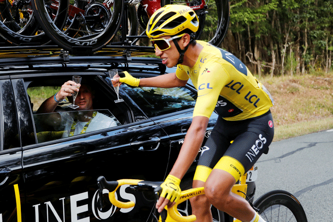Team INEOS rider Egan Bernal of Colombia, wearing the overall leader's yellow jersey, toasts champagne at the car of his team director after his Tour de France victory