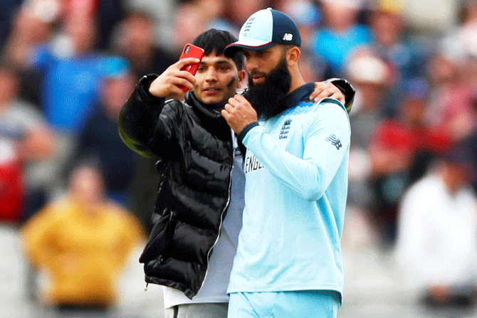 A pitch invader poses for a selfie with England's Moeen Ali at the end of the match