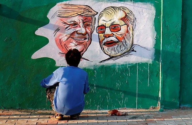 A man applies finishing touches to paintings of US President Donald Trump and India's Prime Minister Narendra Modi on a wall.