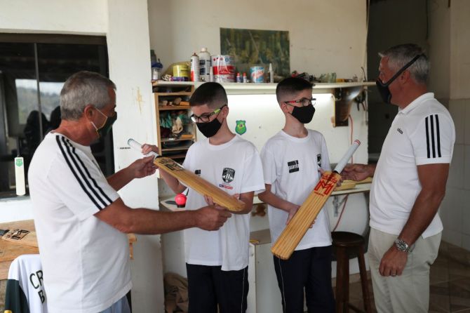 Luiz Roberto Francisco and Matt Featherstone give bats as a gift to budding cricketers Bernardo and Breno Bagatin Passoni
