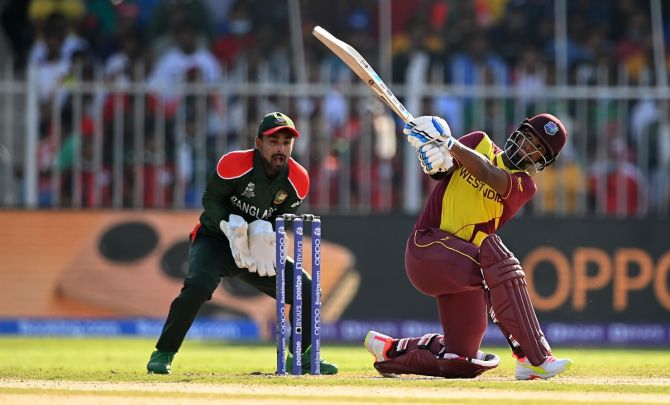 West Indies batter Nicholas Pooran hits a six as Bangladesh wicketkeeper Liton Das looks on. 
