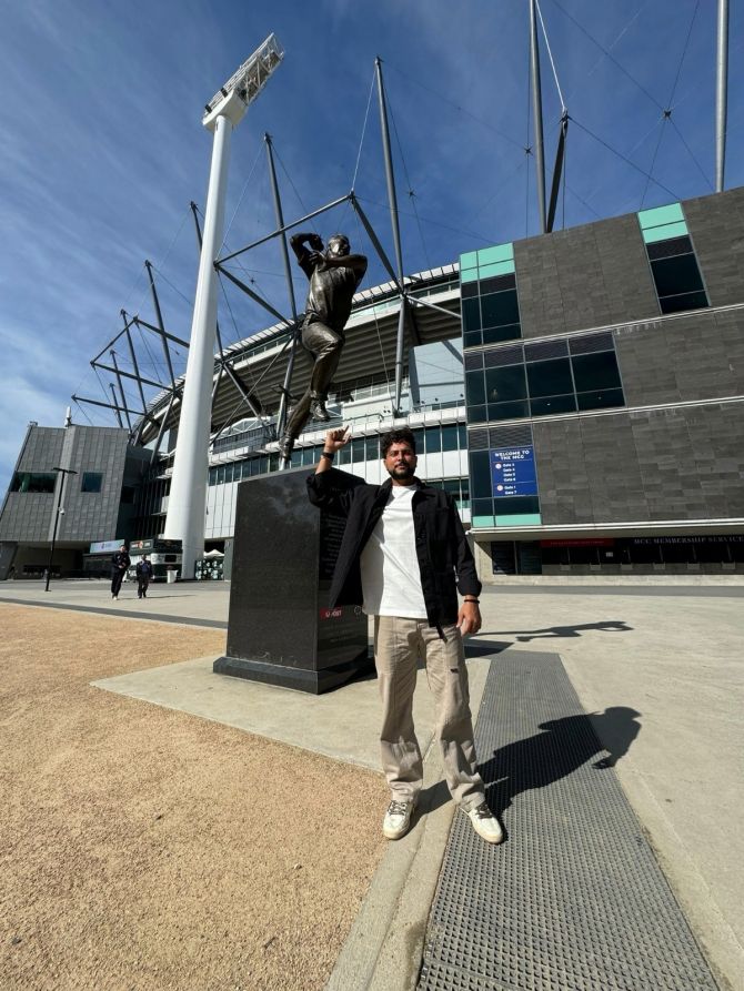 Kuldeep Yadav stands with Shane Warne's statue in the background, outside the MCG, in Melbourne