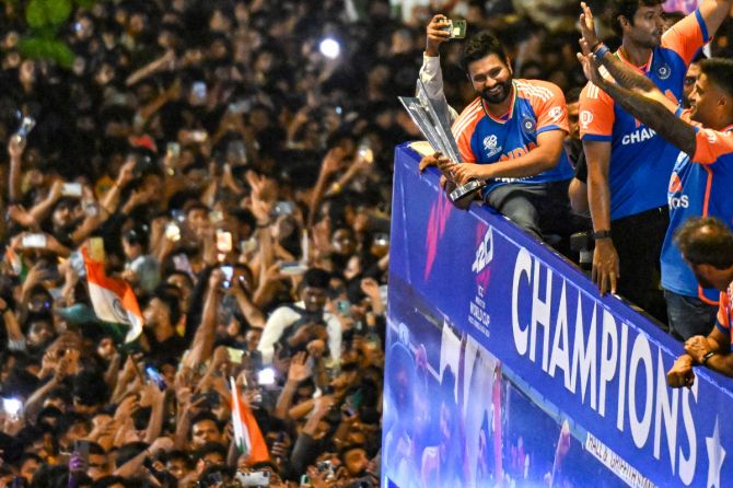 Rohit Sharma celebrates with the trophy atop the bus during the victory parade, surrounded by a sea of fans, on Thursday
