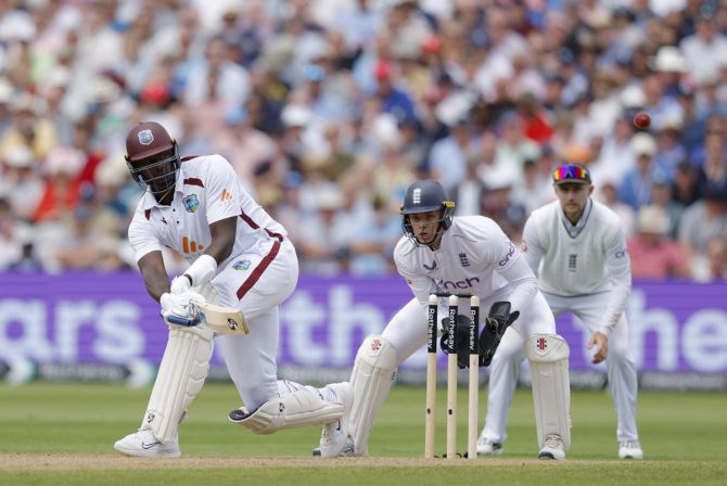 Jason Holder sweeps the ball to the boundary as England wicketkeeper Jamie Smith looks on.