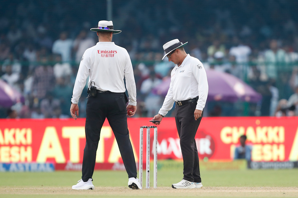 Umpires use a light meter to check the light on the field before rain halts play on Day 1