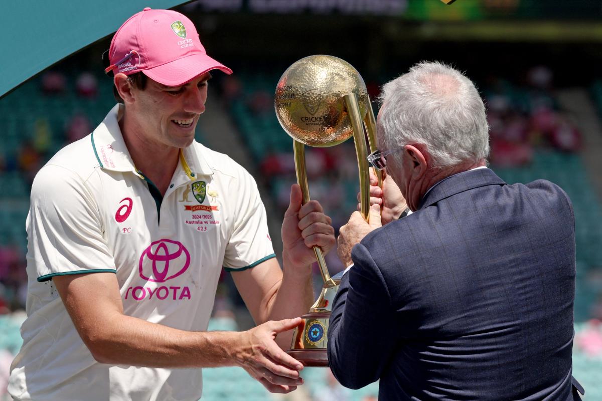 Pat Cummins receives the trophy at the hands of Allan Border