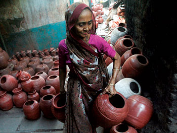 A woman carries newly-created clay water pots after drying them at a slum in Mumbai