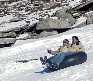 Tourists slide on a snow covered mountain of Rohtang Pass in the