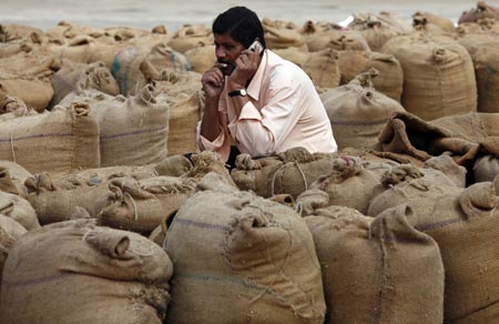A man speaks on a mobile phone amid sacks filled with wheat and rice inside the market yard of the Agriculture Product Marketing Committee (APMC) on the outskirts of the western Indian city of Ahmedabad November 25, 2010. India's food price index rose 10.15 percent, government data on Thursday showed.