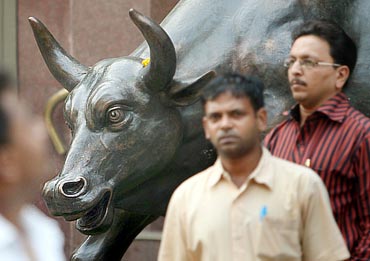 People walk past a bronze replica of a bull at the Bombay Stock Exchange (BSE) building in Mumbai