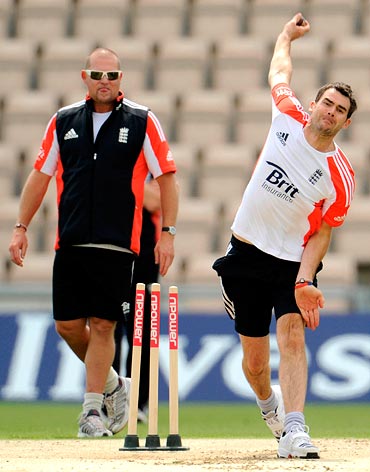 England's James Anderson bowls watched by bowling coach David Saker (L) during a training session