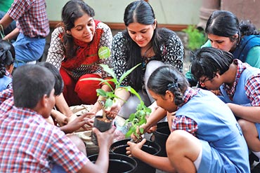 Two young women from iVolunteer engage students in planting saplings