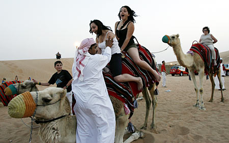 A keeper helps tourists dismount from a camel in the Dubai desert