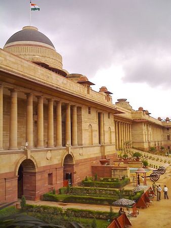 India's tricolour flutters on top of the Rashtrapati Bhavan that stands against a cloudy sky.
