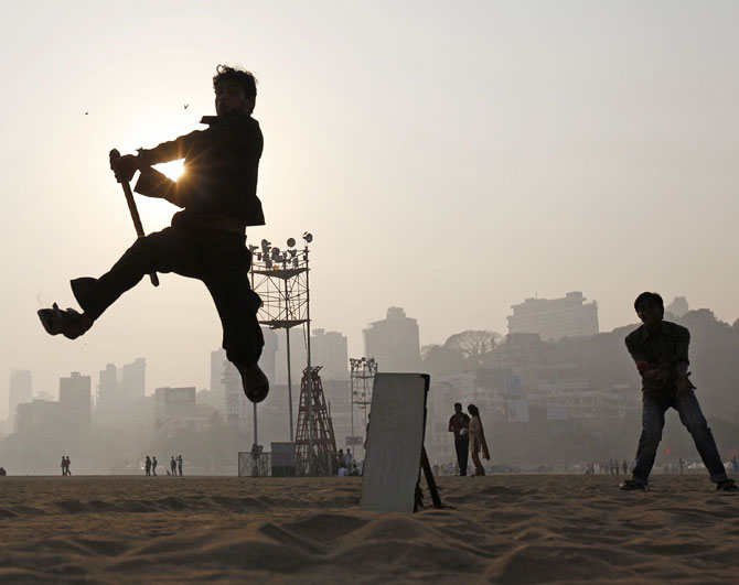 A man jumps in the air to hit a ball as people play cricket by the beach with an improvised stick for a bat and a piece of wood for wickets in Mumbai.