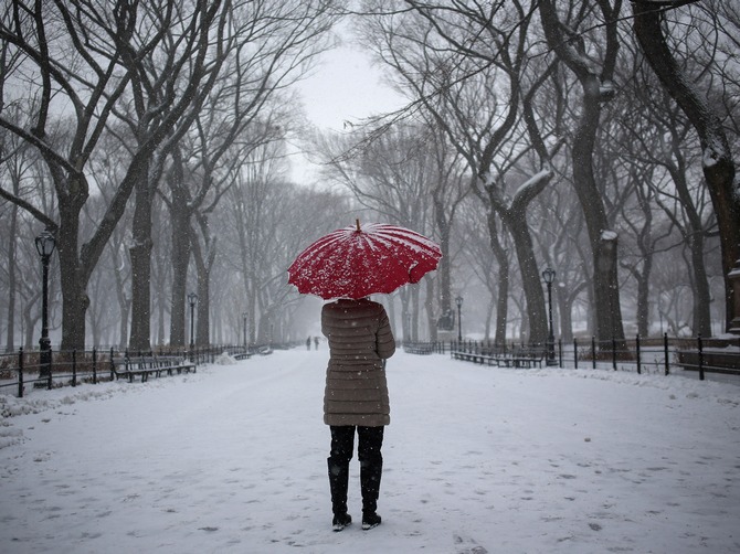 A woman stands with an umbrella during snowfall at Central Park in New York.