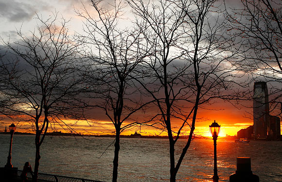 A woman stops to watch the sun set over New Jersey from Battery Park in New York