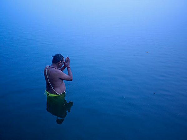 Hindu devotee stands in the waters of river Ganges to offer prayers to Sun god at dawn in Varanasi.