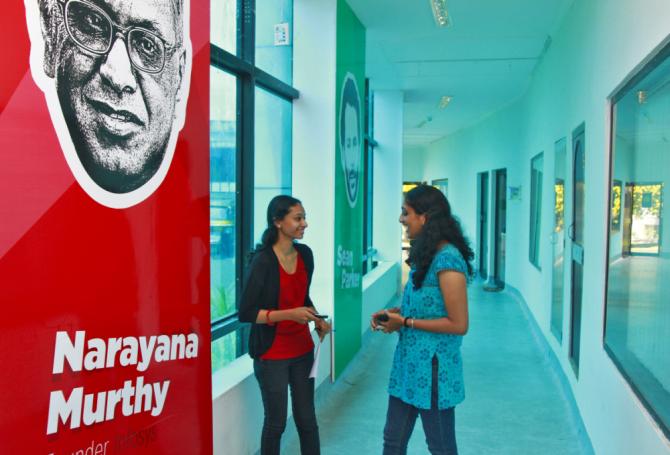 Employees talk as they stand next to flex board poster of Infosys founder Narayana Murthy at the Start-up Village in Kinfra High Tech Park in the southern Indian city of Kochi