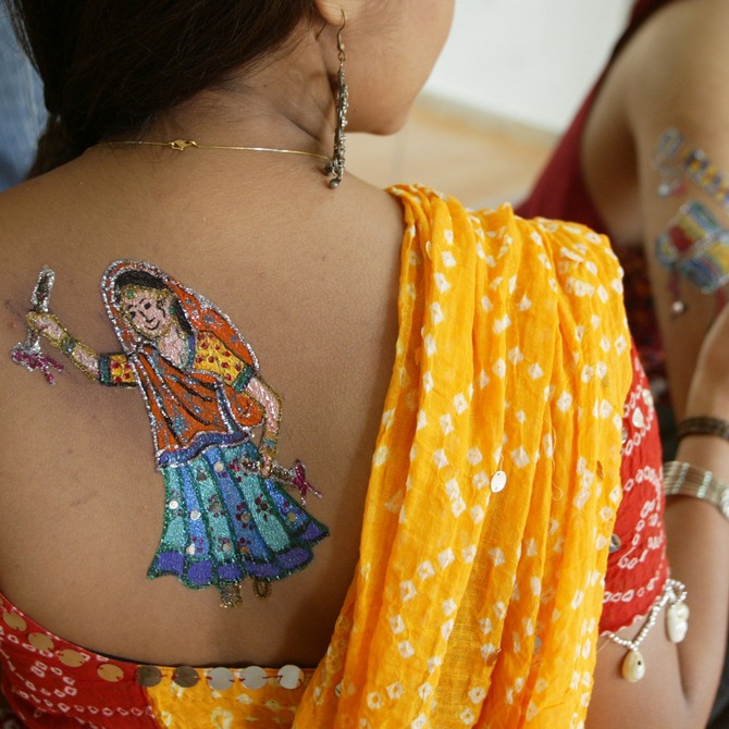 An Indian model (L) has a picture of a traditional Garba dancer painted on her back, as another gets hers painted.