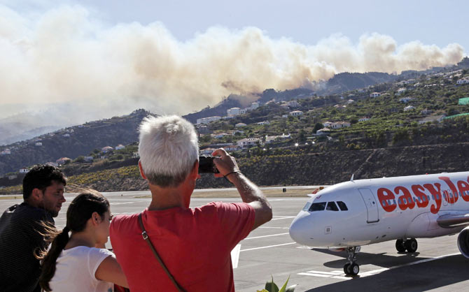 Tourists take photos of forest and bush fires on the mountains on the Portuguese island of Madeira island while waiting for the local airport to re-open July 19, 2012.