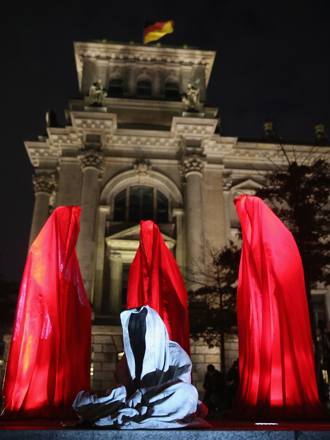 Illuminated sculptures of cloaked figures in red surround one that is seated outside the Reichstag as part of the Festival of Lights on October 14, 2013 in Berlin, Germany. Landmarks across the city are illuminated in colors and patterns in the annual Festival of Lights that always takes place in October.