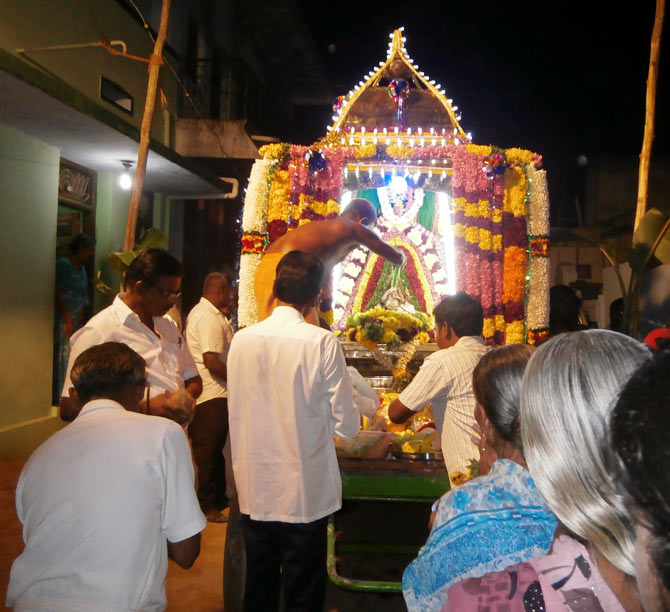 A priest conducts a pooja as people stop to offer their prayers