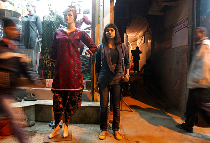 A young girl stands outside a store in New Delhi selling traditional Indian outfits.